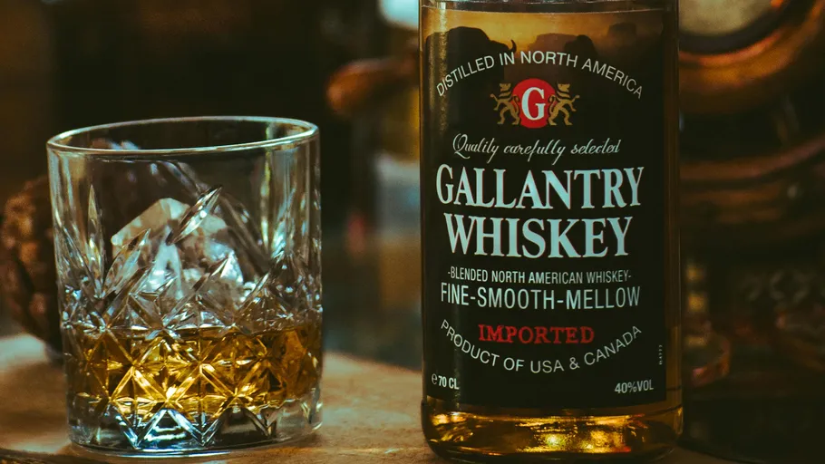 A whiskey glass with whiskey stands in front of a bottle.