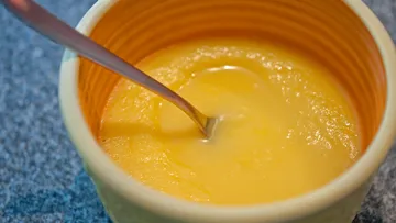 Yellow pudding in a bowl stirred with a spoon.