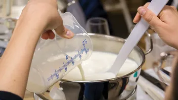 Eine Hand gießt Milch in einen Topf zum Kochen.