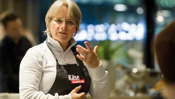 Frau erklärt Käse in einem modernen, hellen Raum.