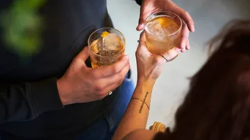 Two hands hold drinks with ice and orange peel.