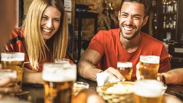 Two smiling people are sitting at a table with beer.