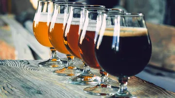 Sechs Gläser Bier stehen auf einem Holztisch.