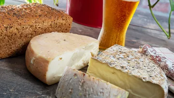 Cheese and bread lie on a wooden tray next to a beer glass.
