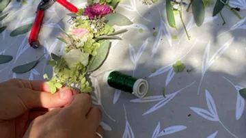 Hands tie flowers with green thread on the table.