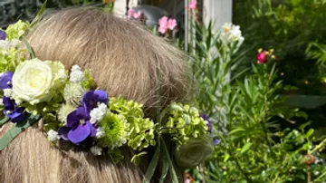 Flower wreath on hair, surrounded by colorful plants.
