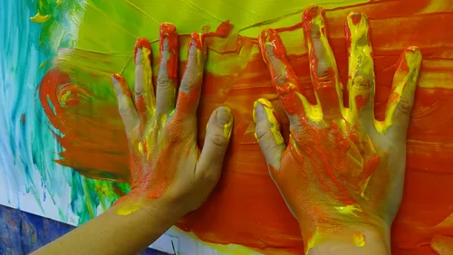 Hände malen rote + gelbe Farbe auf Papier, kreative Aktivität.