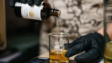 The bottle pours oil into a measuring cup on a scale.