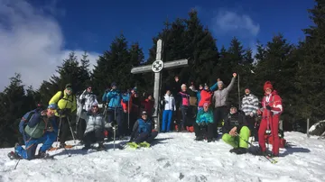 Gruppe von Menschen posiert am Gipfelkreuz im Schnee.
