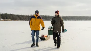 Zwei Männer gehen auf zugefrorenem See mit Ausrüstung.