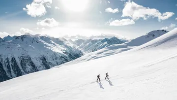 Zwei Wanderer gehen über eine verschneite Berglandschaft.