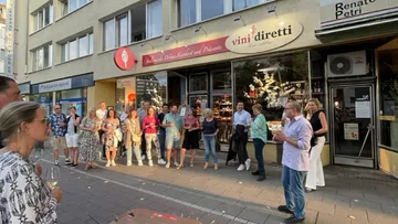 Group of people having drinks in front of a wine shop.