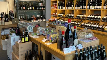 Wine bottles are on shelves and tables in a shop.