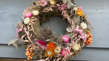 Bunter Kranz aus Trockenblumen, auf grauem Hintergrund präsentiert.
