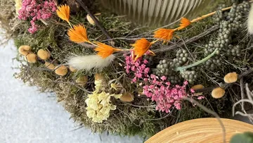 Trockenblumen und Pflanzen dekorieren eine grüne, moosige Oberfläche.