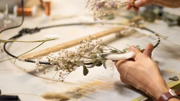 Flower arrangement is created by hand on a table.