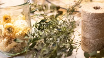 A jar of dried flowers stands next to plants and twine.