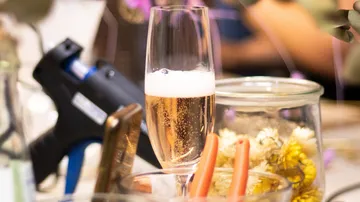 Champagne glass is placed on the table between flowers and tools.