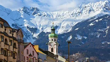 Berglandschaft mit schneebedeckten Gipfeln und Stadtarchitektur.