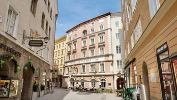 Engstraße mit historischem Hotel und Cafés im Freien.