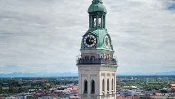 Clock tower shows the time, surrounded by urban landscape and mountains.
