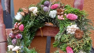 Wreath of green branches and colorful dried flowers hangs.