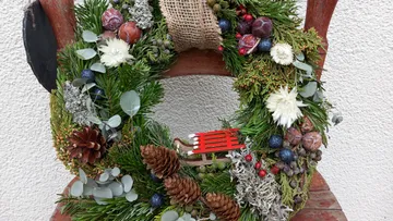 Wreath of green branches decorated with flowers and pine cones.