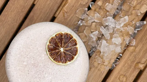 Drink with dried lime is lying on a wooden surface next to ice.