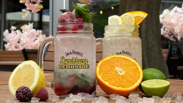 Zwei Gläser mit Limonade, Fruchtstücken und Minze bei Sonnenschein.