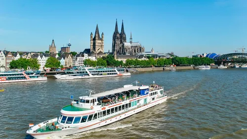 A ship sails on a river surrounded by an urban landscape.