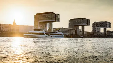 A boat sails in front of modern buildings on the water.
