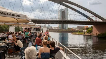 Ship with guests enjoying views under a bridge.