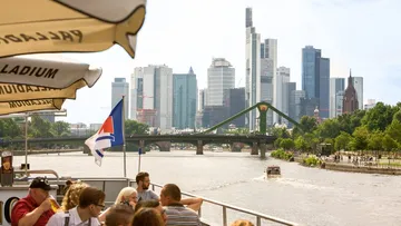 Frankfurt skyline, boat sails through the river in sunshine.
