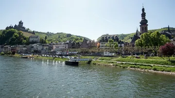 River bank with houses, rows of trees and a castle in the background.