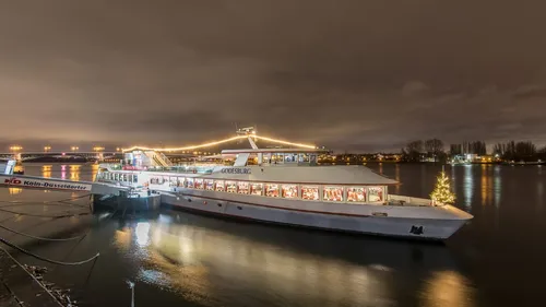 An illuminated boat is situated on a quiet riverbank.