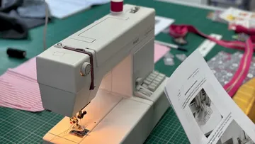 Nähmaschine näht an einem grünen Tisch mit Zubehör.