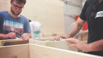 Two people work together on wooden structures in a workshop.