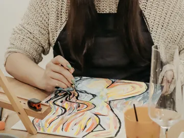Woman paints vivid colors on paper, table environment, glasses.