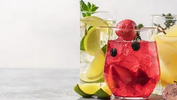 Colourful cocktails sit on a table with fruit.