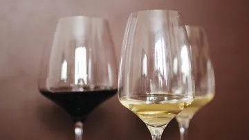 Three wine glasses standing, one filled with red wine.