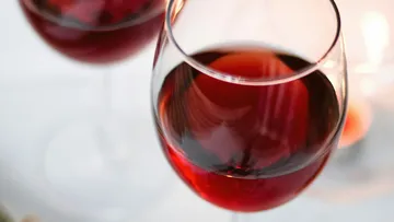 Rote Weingläser stehen auf einem Tisch, Kerzenlicht reflektierend.