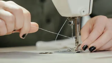 Eine Hand führt Faden durch eine Nähmaschine in einem Raum.