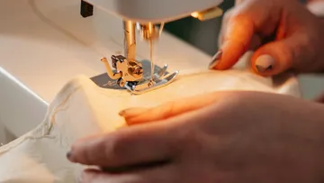 Nähmaschine näht Stoff unter einer Hand. Helle Umgebung.