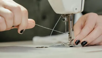 Sewing machine sews fabric while the hand holds the thread.