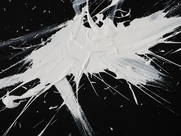 Weißer Farbklecks spritzt auf schwarzem Hintergrund.