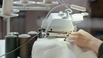 Sewing machine sews fabric in a well-lit room.