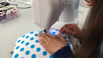 Sewing machine sews blue polka dot fabric in bright surroundings.