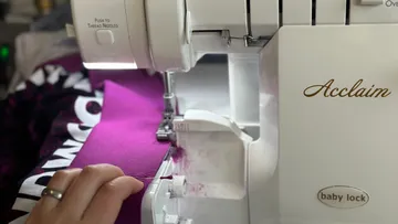 Nähmaschine näht lila Stoff in einem kreativen Raum.