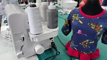 Nähmaschine neben einem bunten Kinder-T-Shirt auf Tisch.