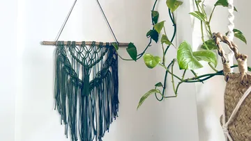 Wandbehang aus Makramee hängt neben einer Pflanzenranke.